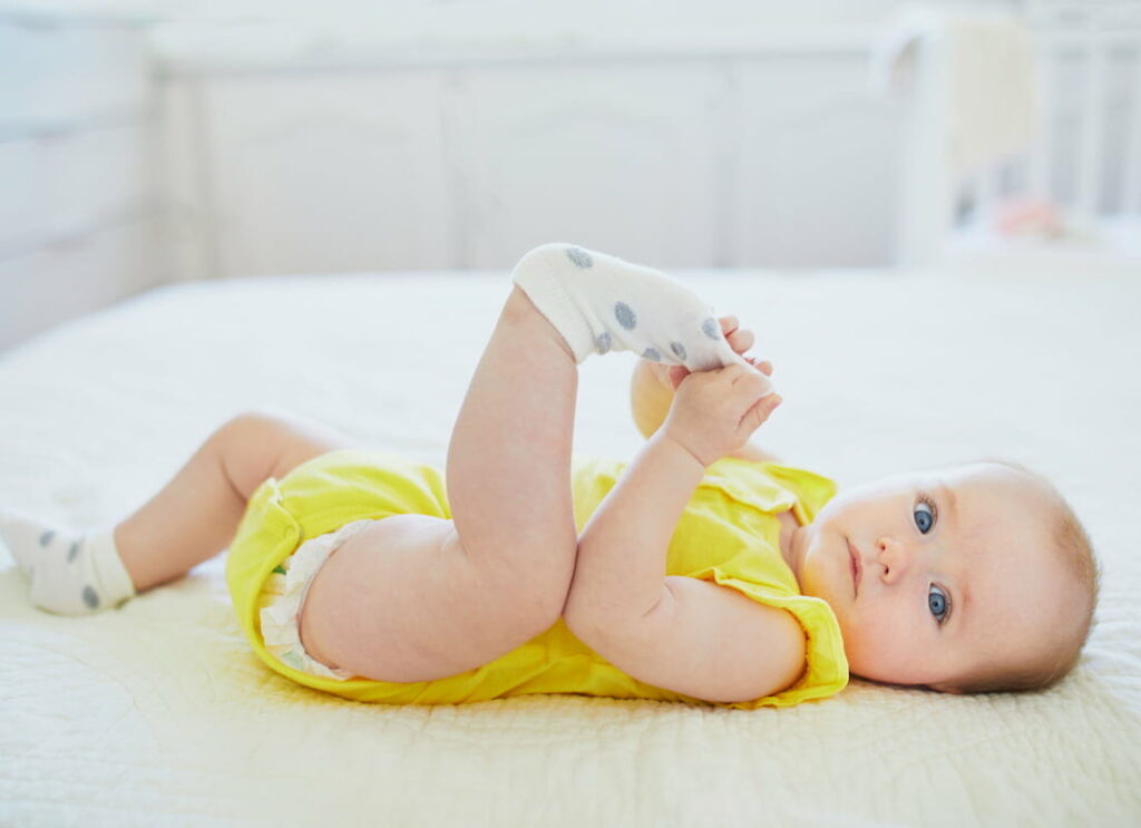A baby lying down whilst holding their sock