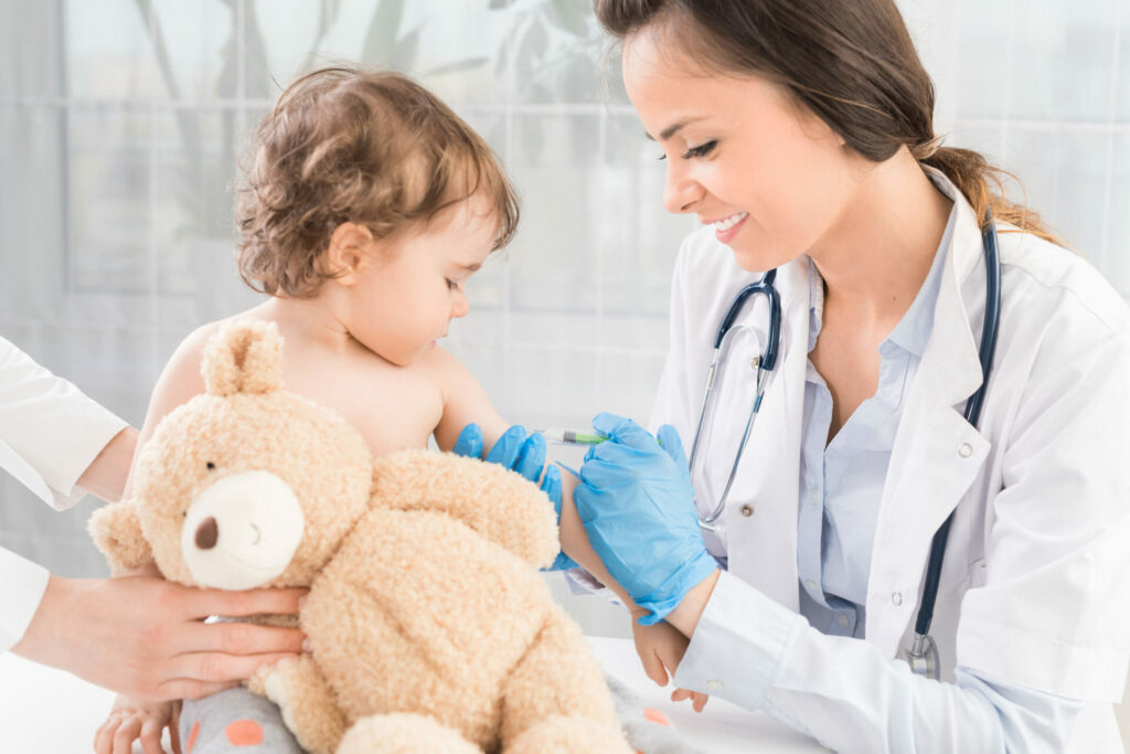 a little baby being vaccinated whilst being comforted by a toy bear