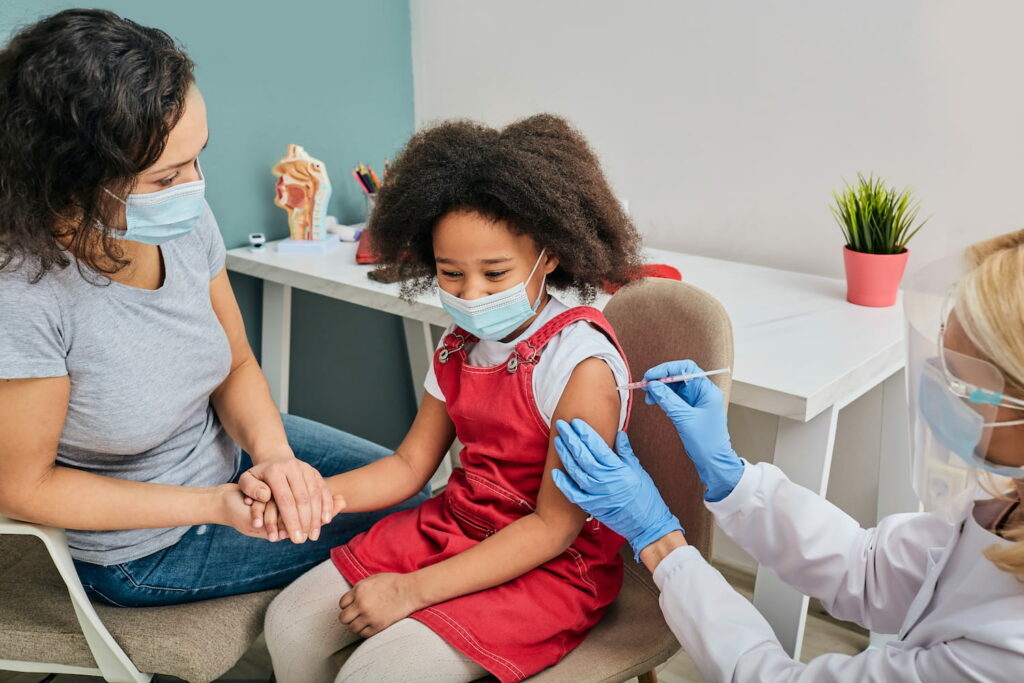 A child receiving a jab in their arm whilst their mother comforts them