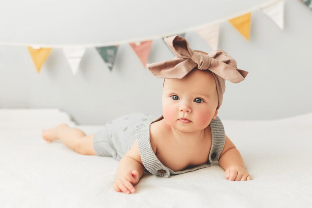 a baby with rosy cheeks lying on their front and looking into the camera