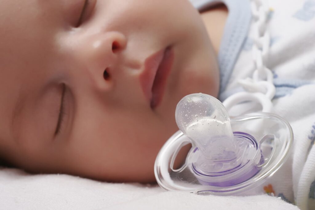 A close up of a baby sleeping next to their dummy