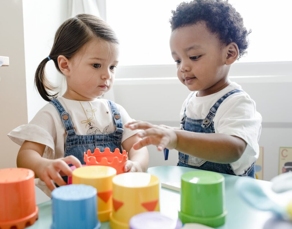 Two toddlers in denim dungarees playing with cups